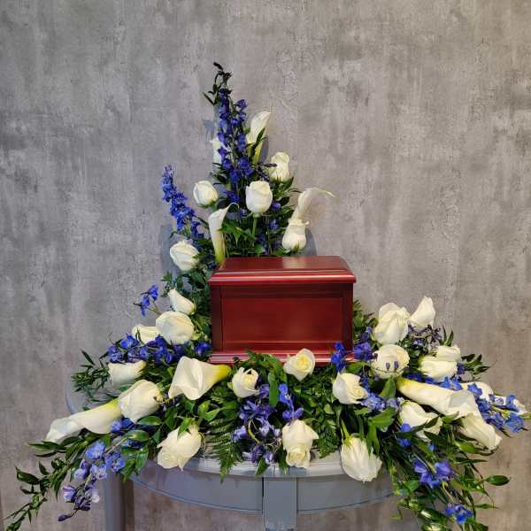White roses and blue flowers arranged around a red urn on a table