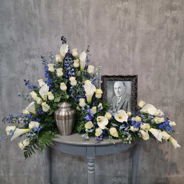 White calla lilies and roses arranged around a framed portrait and urn.