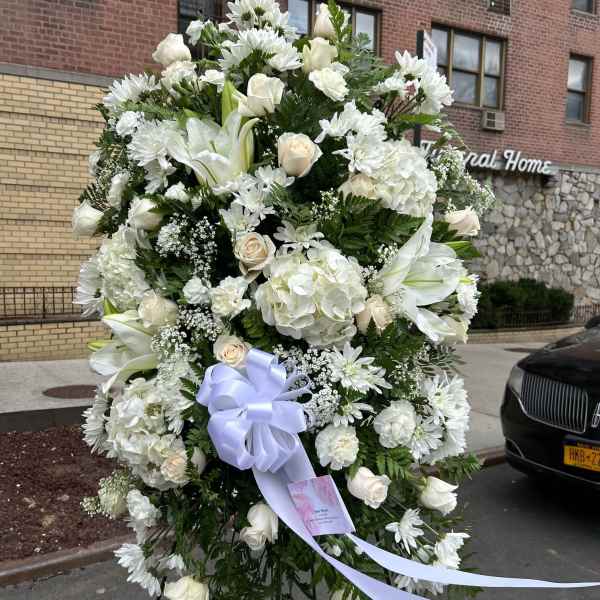 Large white funeral wreath with roses, lilies, and daisies on an easel