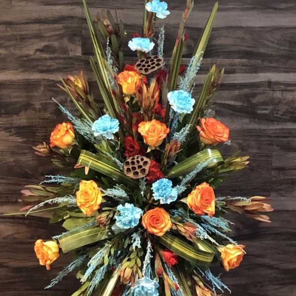 Tall floral spray with orange roses and blue accents on a stand