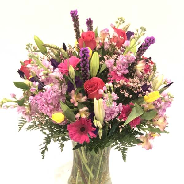 Mixed bouquet of pink, purple, and yellow flowers in a glass vase