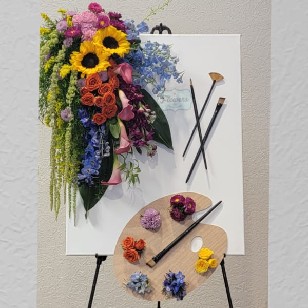 Colorful floral arrangement on a white canvas with paintbrushes and palette