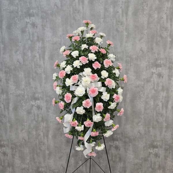 Standing floral spray of pink and white carnations with a white ribbon
