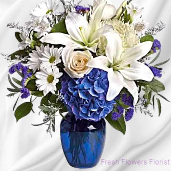 White lilies and daisies with blue hydrangea in a blue vase