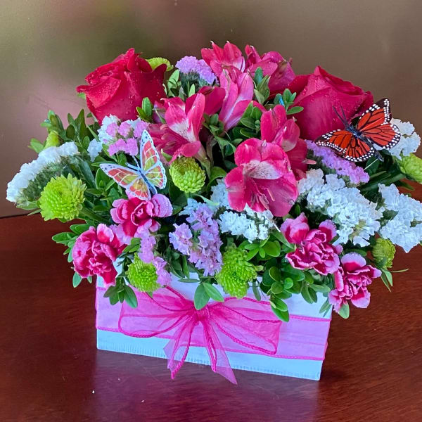 Pink and white floral arrangement in a gift box beside a lit red candle in a glass holder