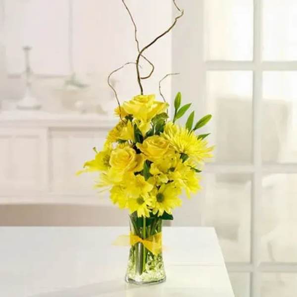 Yellow flower arrangement in a clear glass vase with curly branches