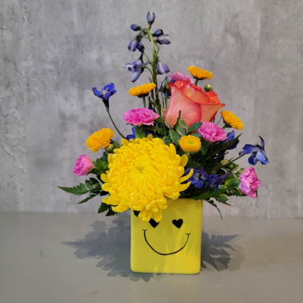 Colorful bouquet in a yellow smiley-face vase with a peach rose and yellow chrysanthemum