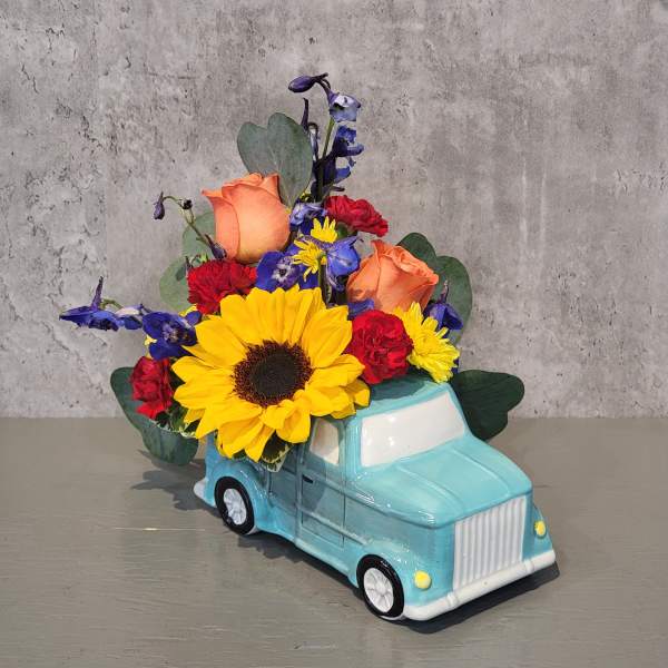 Flower arrangement in a blue truck-shaped container with sunflowers and roses