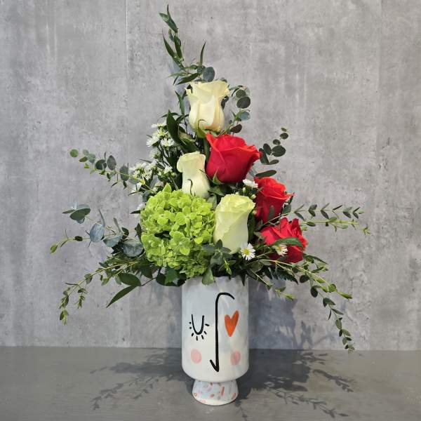Tall floral arrangement with red and cream roses in a painted vase