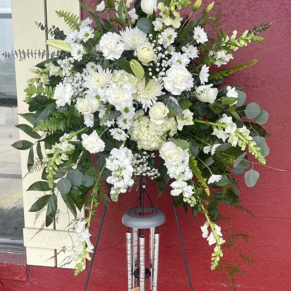 Large white funeral spray on a black easel with wind chimes below