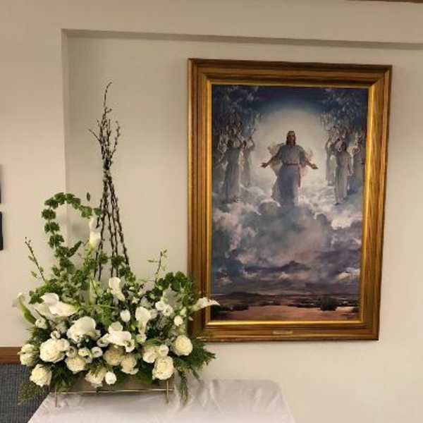 White floral arrangement on a stand beside a framed painting