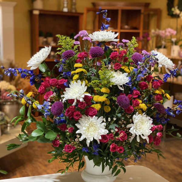 Large mixed flower arrangement in a white vase with pink, white, yellow, and purple blooms.