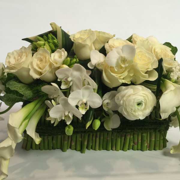 White floral arrangement with roses, orchids, calla lilies, and ranunculus in a low rectangular base