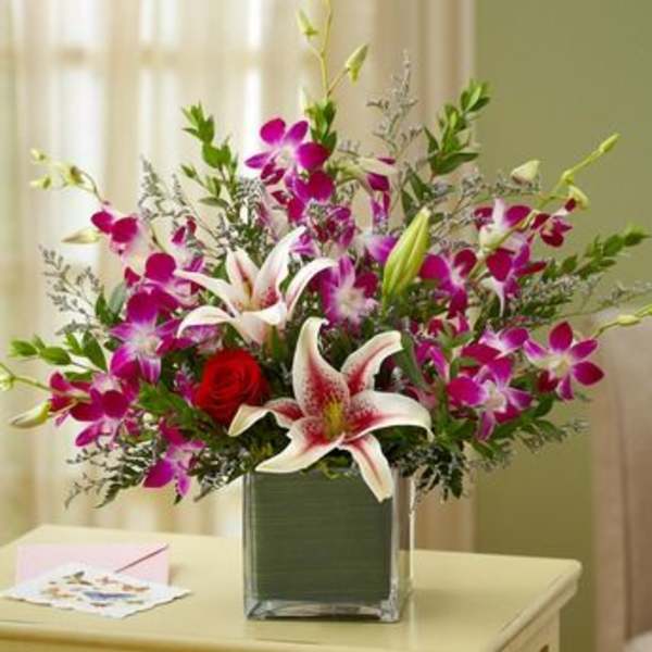 Bouquet of pink orchids, lilies, and a red rose in a square vase