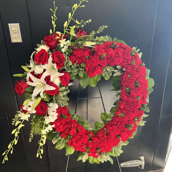 Heart-shaped red floral wreath on a stand with white lilies and roses