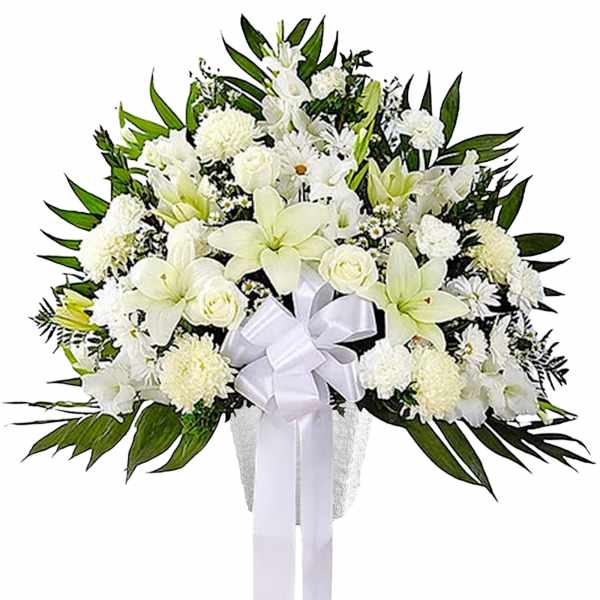 White funeral spray with lilies, roses, and a ribbon on a stand