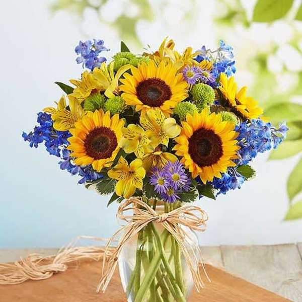 Bouquet of sunflowers, blue flowers, and yellow blooms in a glass vase