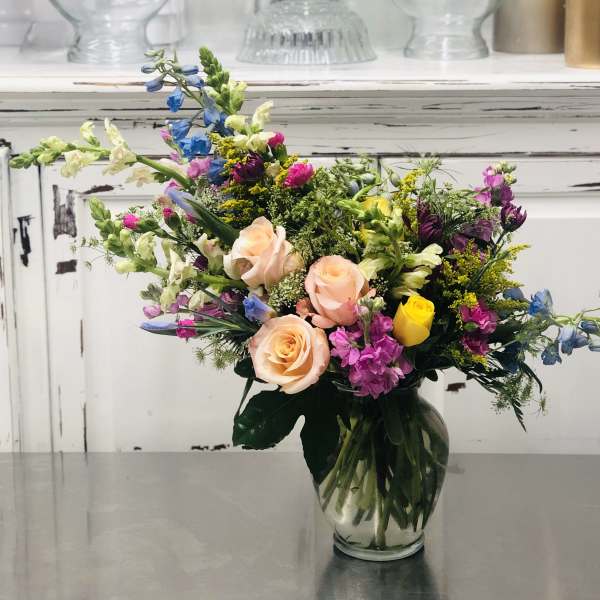 Mixed bouquet of roses and colorful flowers in a clear glass vase