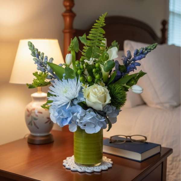 Bouquet of blue and white flowers in a green vase on a bedside table