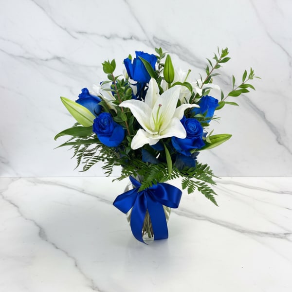 Blue roses and white lilies in a glass vase with a blue ribbon