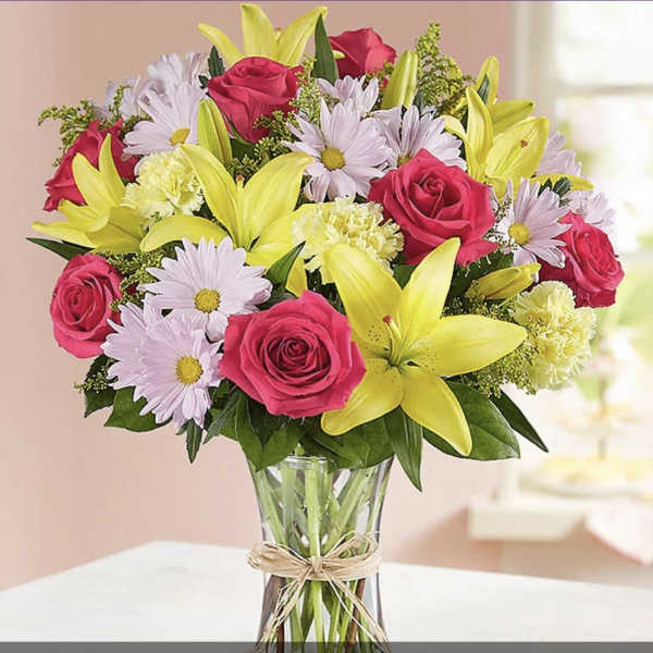 Bouquet of pink roses, yellow lilies, and pale daisies in a glass vase