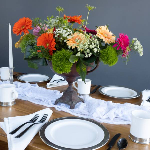 Colorful gerbera daisy centerpiece in a dark pedestal vase on a set dining table