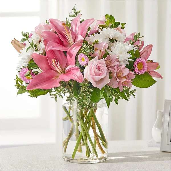 Pink lilies and roses in a clear glass vase with white daisies