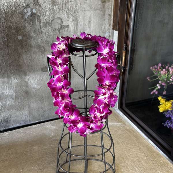 Magenta orchid lei draped over a black metal stand