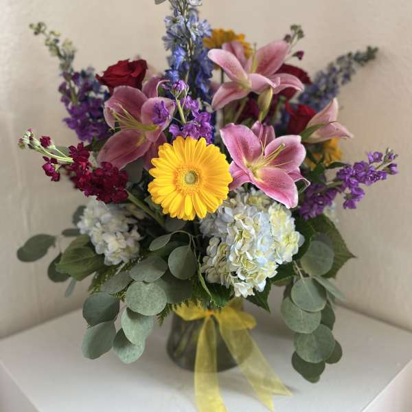 Mixed bouquet with pink lilies, yellow gerbera daisy, hydrangeas, and purple flowers in a vase