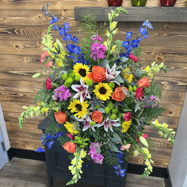 Large standing floral spray with sunflowers, roses, lilies, and blue delphinium