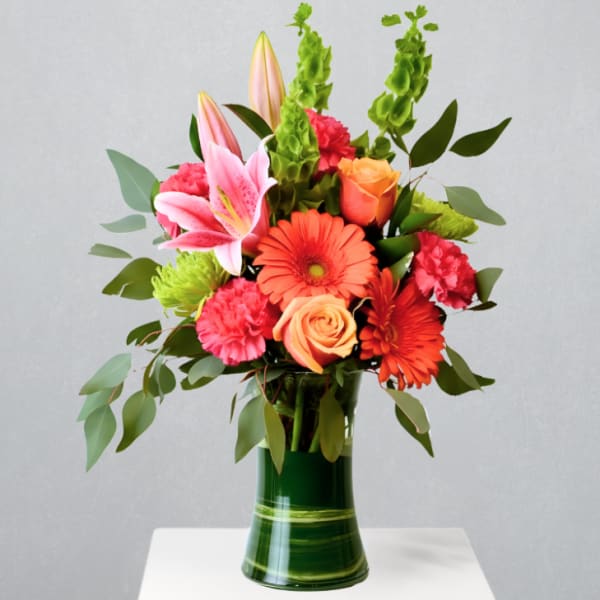 Bright bouquet of lilies, gerbera daisies, roses and carnations in a tall green glass vase