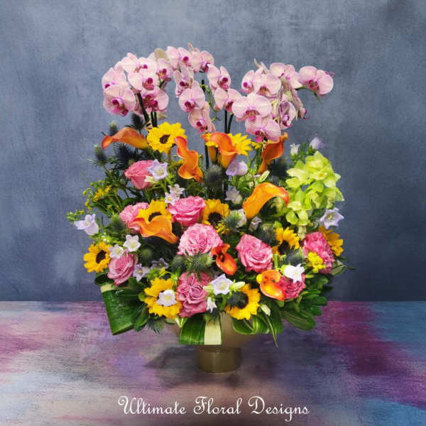 Mixed floral arrangement with pink orchids, roses, calla lilies, and sunflowers in a vase