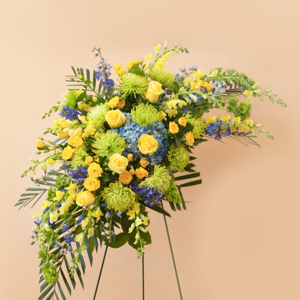 Large floral spray with yellow roses, blue flowers, and green blooms on a stand