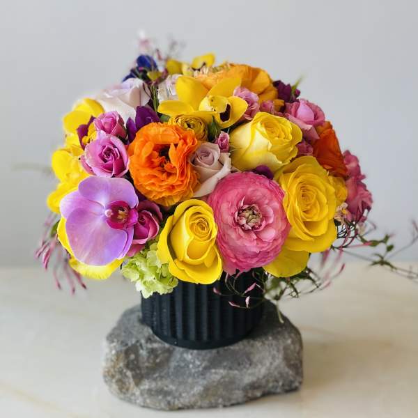 Bright mixed bouquet in a black vase with yellow, pink, orange, and purple blooms.