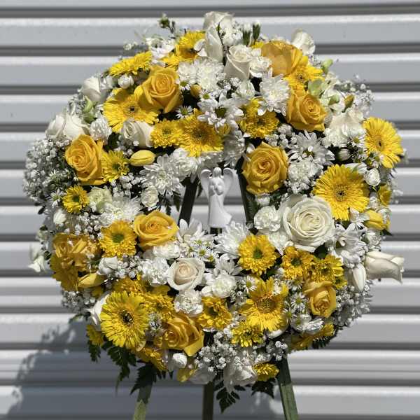 Yellow and white floral wreath on a stand with a small angel figure in the center