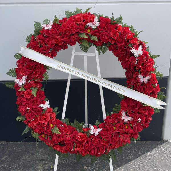 Large red rose funeral wreath on a stand with a white ribbon