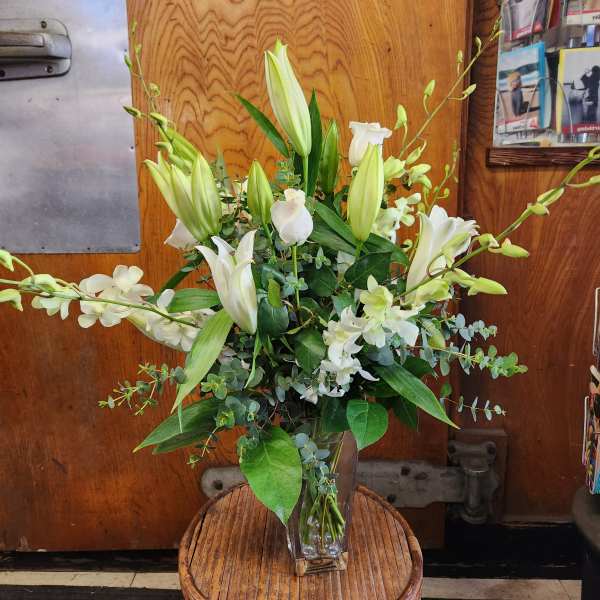 White lilies and orchids arranged in a clear glass vase