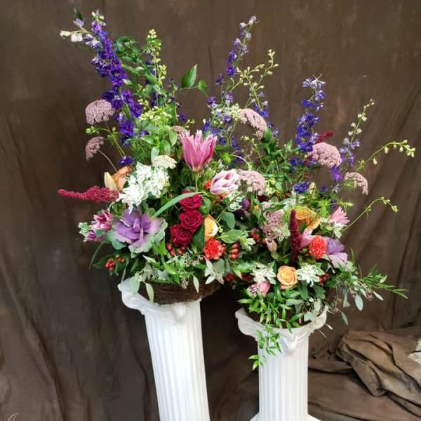 Two tall floral arrangements in white pedestal stands with pink, purple, and red blooms.