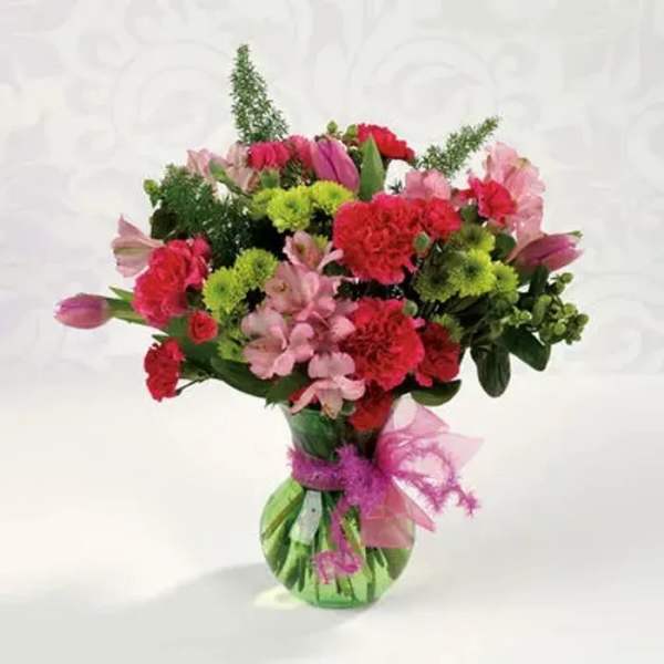 Mixed bouquet of pink and red flowers in a green glass vase