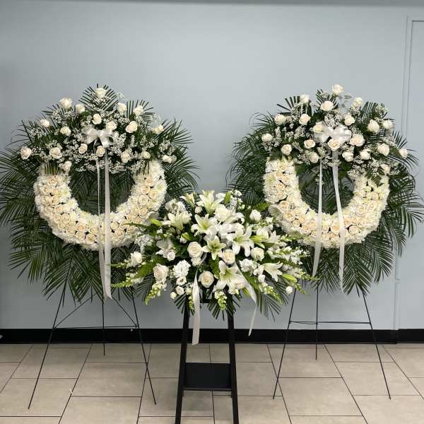 Three white floral funeral wreaths and sprays on stands