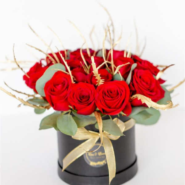 Red roses arranged in a black round box with gold ribbon