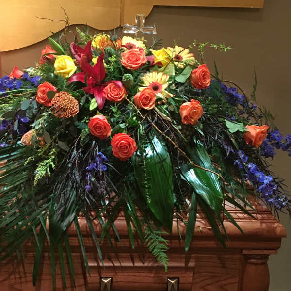 Large casket spray with orange and yellow roses and purple flowers