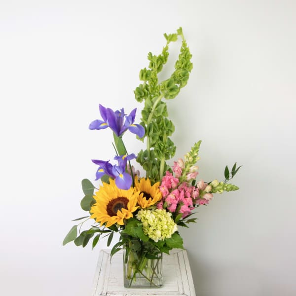 Mixed bouquet with sunflowers, purple irises, pink snapdragons, and hydrangea in a glass vase