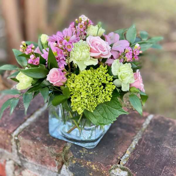 Pink and green floral arrangement in a square glass vase