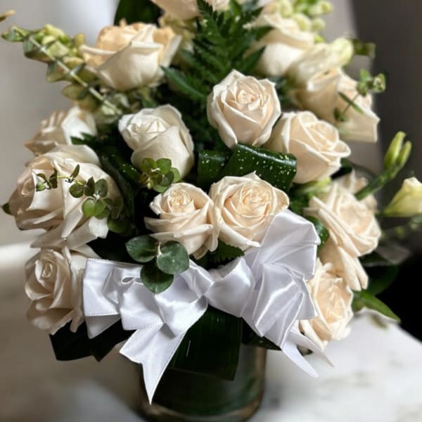 Cream rose bouquet in a glass vase with a white ribbon