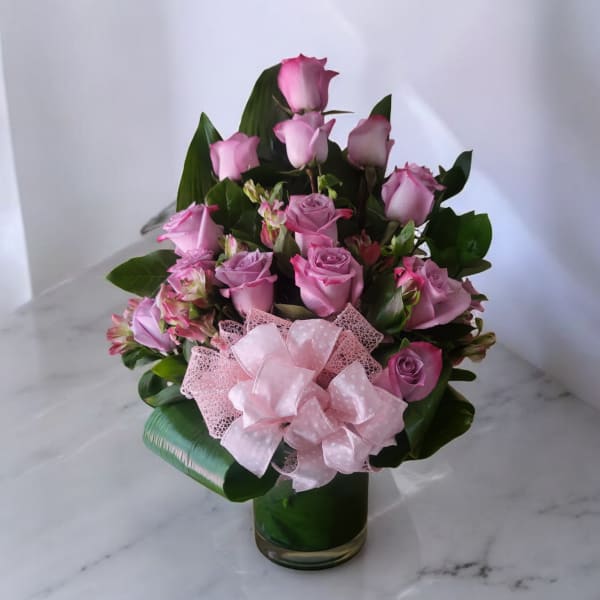 Pink roses arranged in a glass vase with a large pink bow
