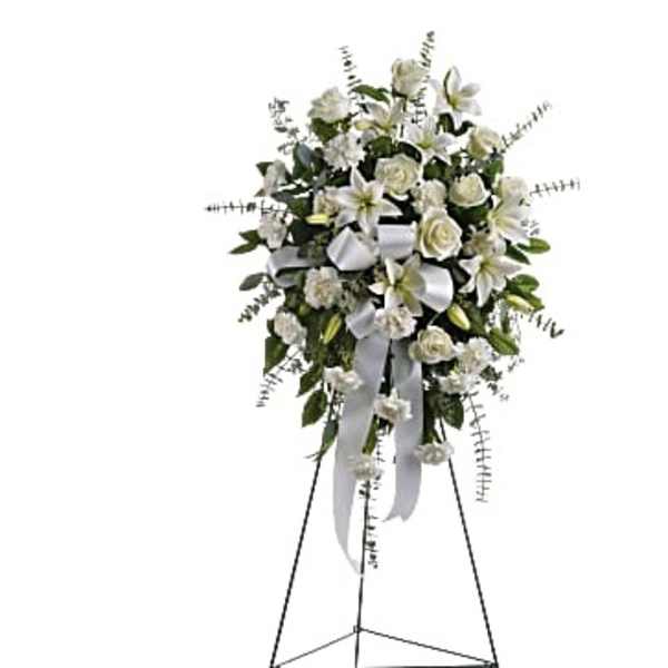 White floral standing spray with lilies, roses, and ribbon on an easel