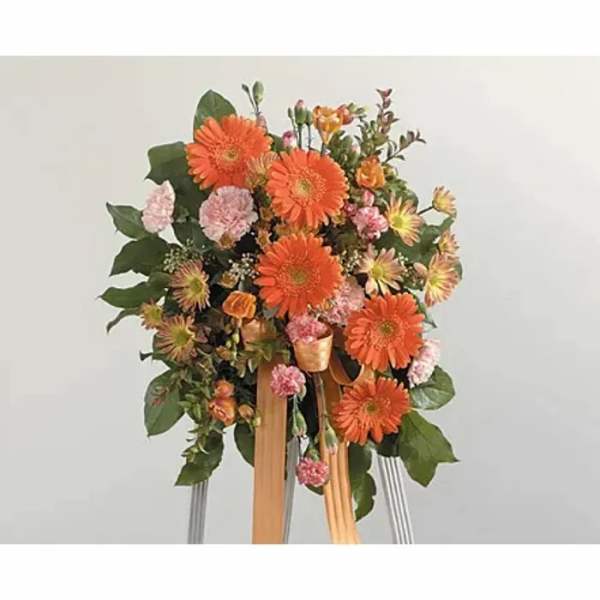 Orange gerbera daisy arrangement with pink accents on a stand