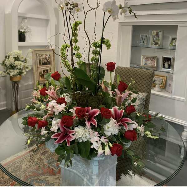 Tall floral arrangement with red roses, pink lilies, and white orchids in a pedestal vase