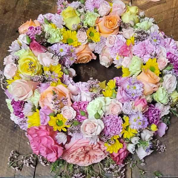 Heart-shaped bouquet of pastel roses and mixed flowers on a wooden surface
